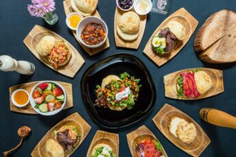 Small wooden patters encircle a central black dish, all full of colourful traditional food at Salmon n Bannock