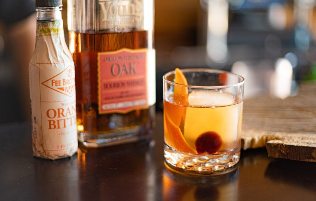 Image of Old Fashioned cocktail in a cut-crystal glass, alongside a bottle of bourbon and a bottle of orange bitters