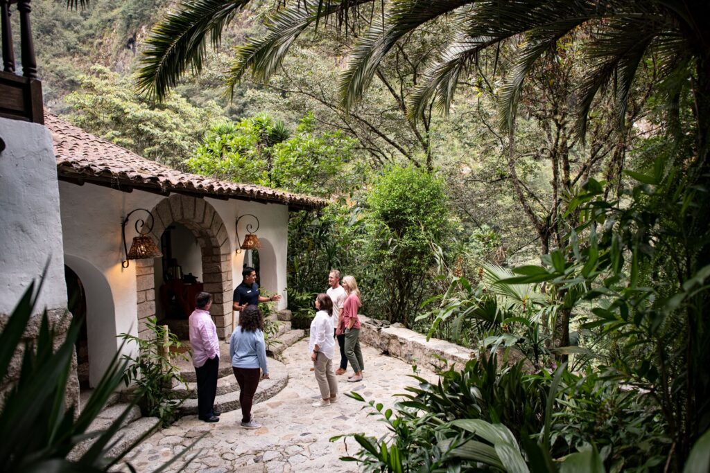 A Travel Concierge talks to guests outside the front of a hotel with rainforest in the background