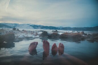 Feet emerging from thermal pool against snowy mountainous landscape