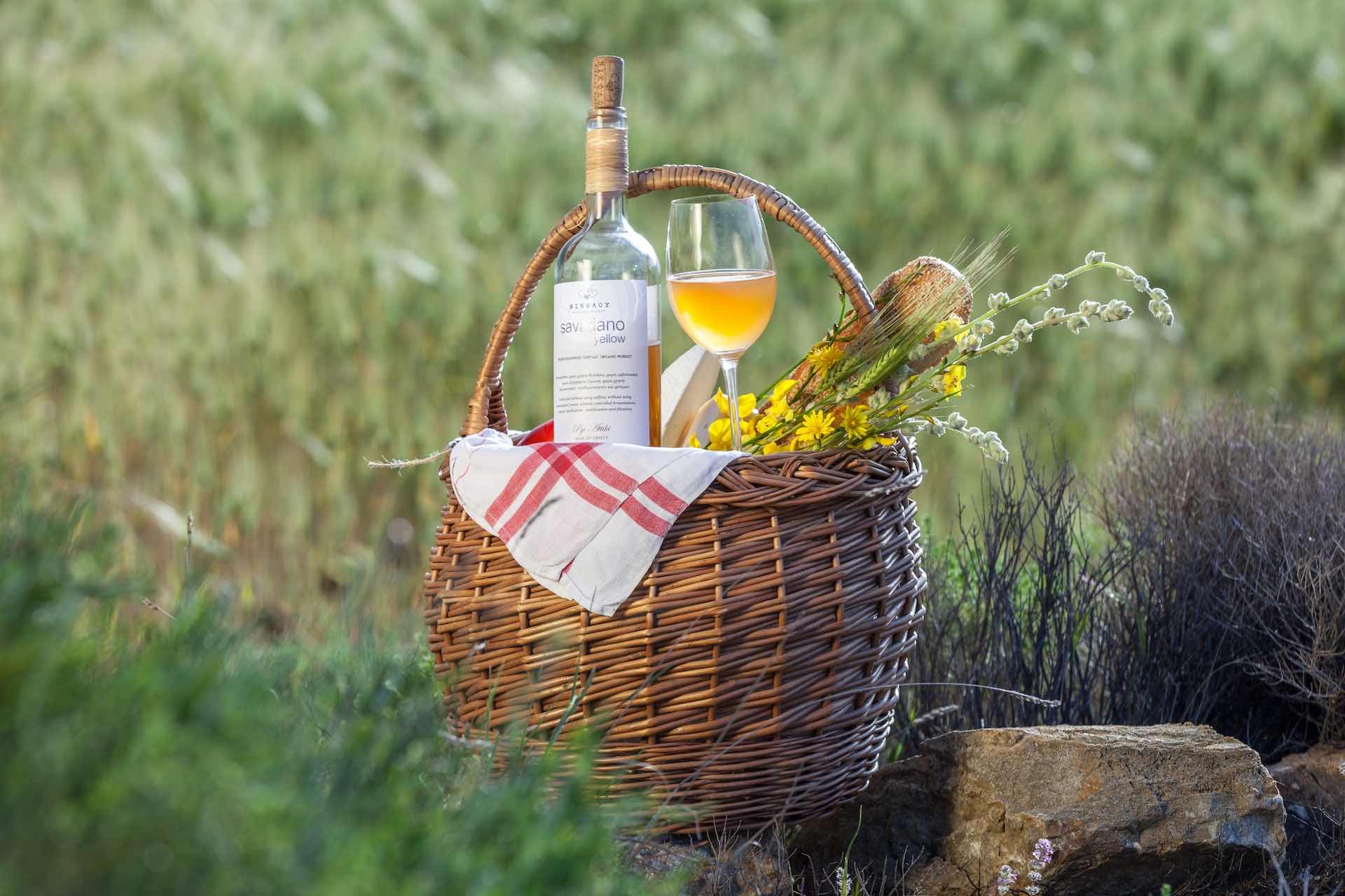 Orange wine glass and bottle on a basket with flowers in a field