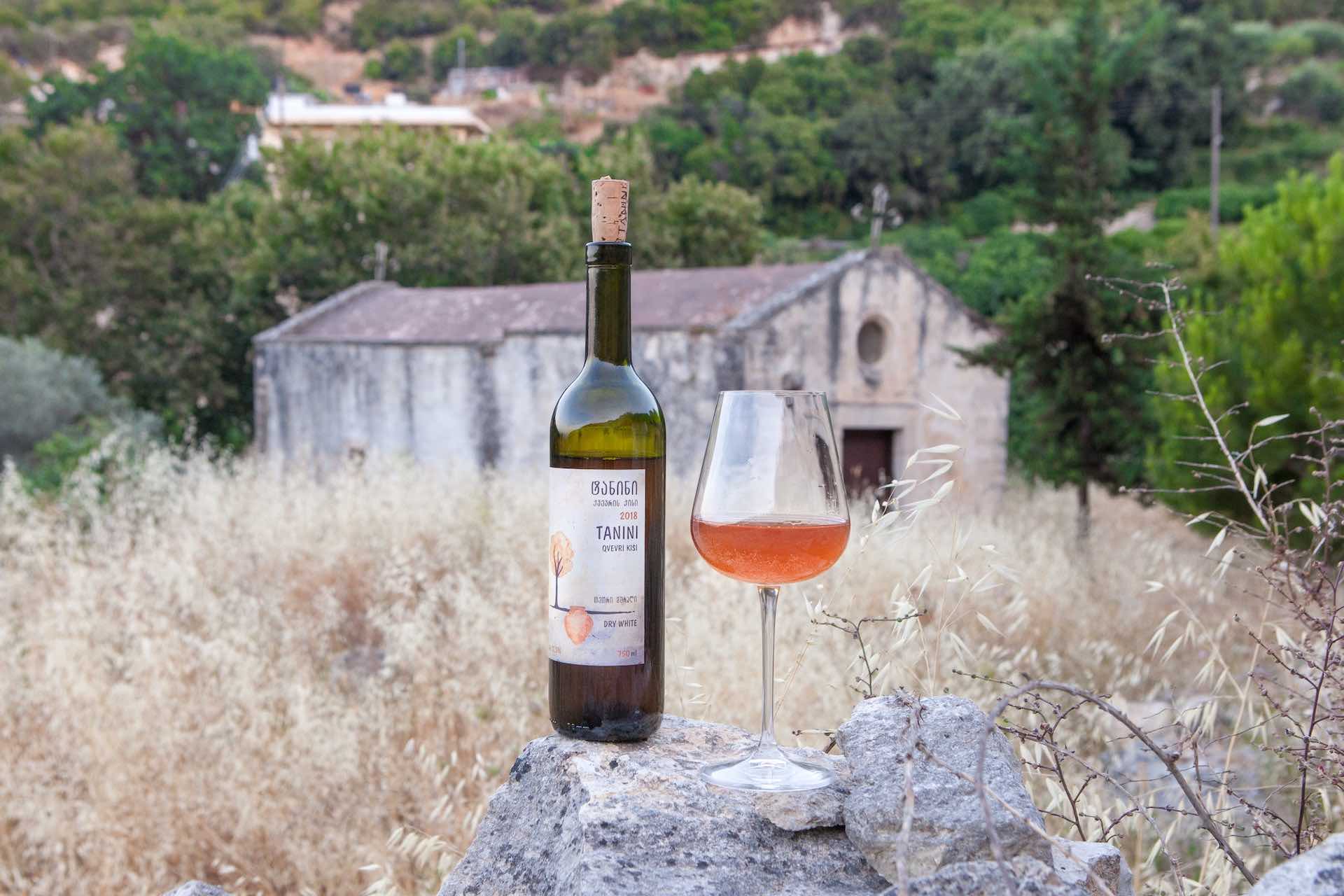 Bottle and glass of orange wine in field with building in background 