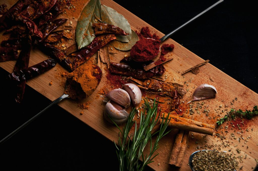 Birds Eye view of red and brown spice powder, green herbs and garlic on a wooden board.