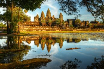 The Angkor Wat temple complex in Cambodia is reflected in the water surrounded by greet trees.