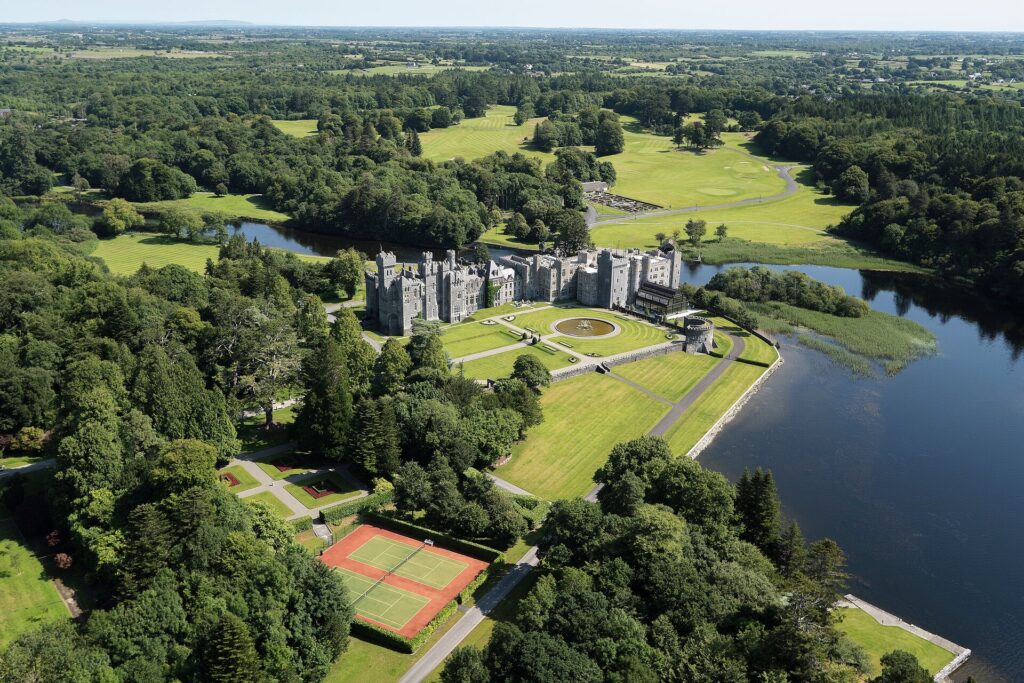 Aerial view of Ashford Castle. whopping the grey stone ramparts set in lush green manicures grounds with woodland on the edges