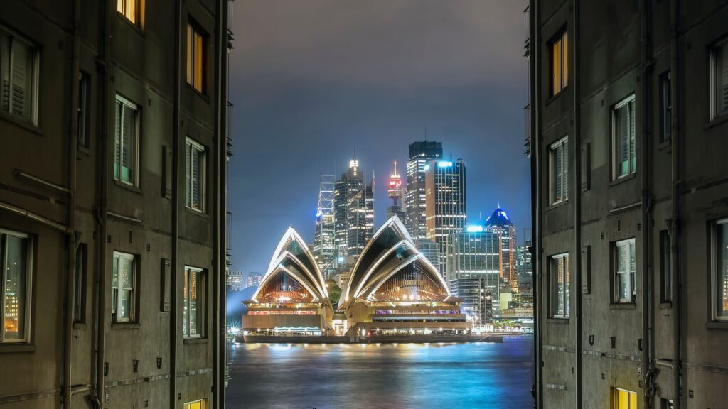 The Sydney Opera House gleams at night, shown from the view between two high buildings