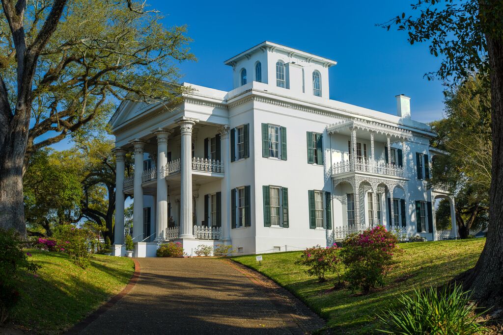 An antebellum house set against a blue sky and green lawn