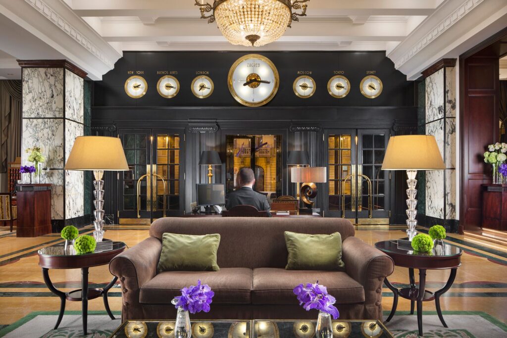 The ornate lobby of the Esplanade Hotel in Zagreb with brown sofas, wooden floors and clocks adorning the walls