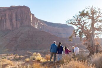 People stadn at the foot of a towering red rock formation in Monument Valley USA