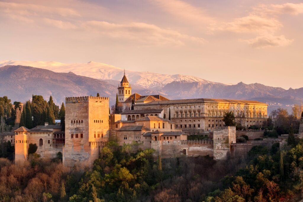 The Alhambra palace seen in early sunlight with snowy mountain peaks in the background