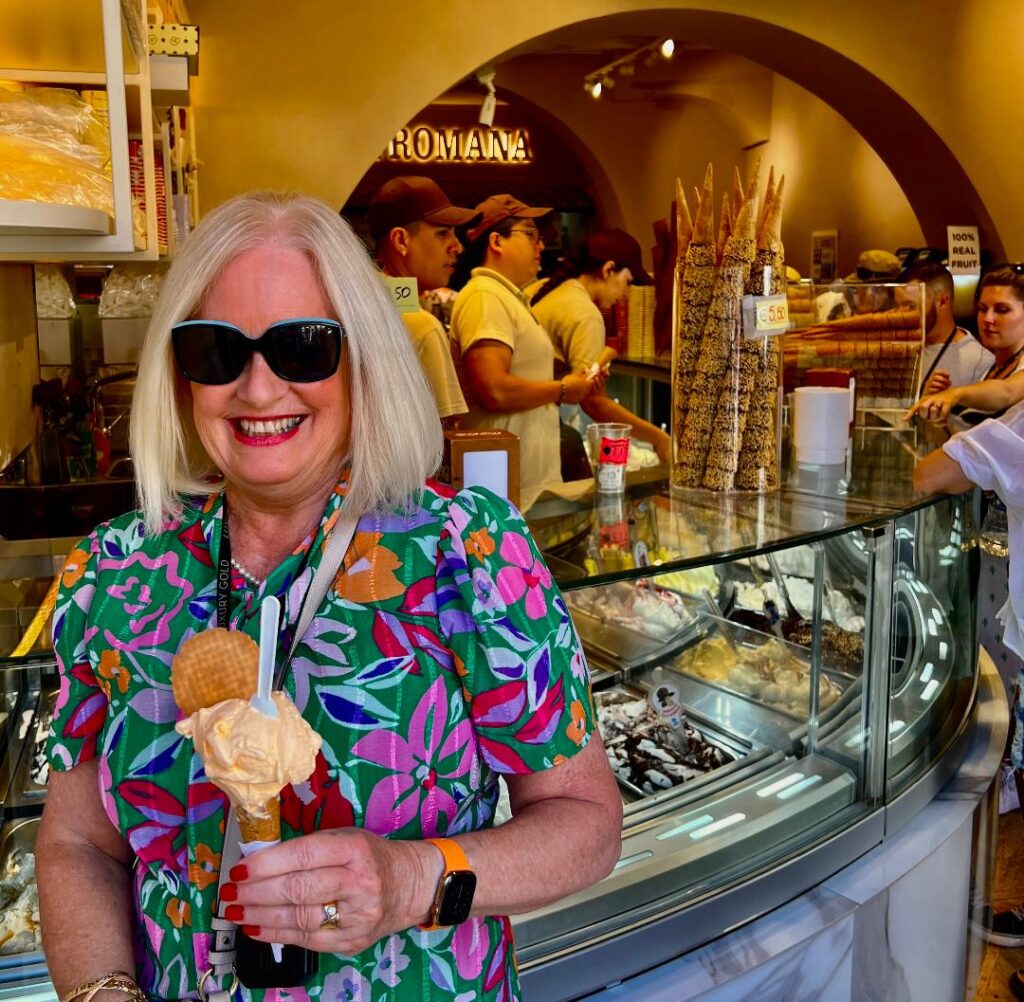 Photo of Dr Sandy at an gelato shop in Italy, holding an ice cream, wearing sunglasses