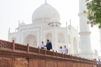 A Luxury Gold Travel Concierge walks with guests in front of the white facade of the Taj Mahal in India.