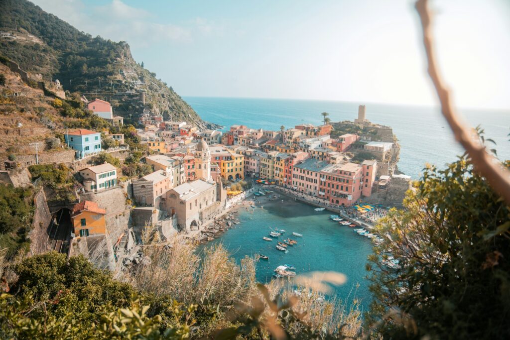 View looking down at one of the villages of Cinque Terre with blue water, fishing boats and a small beach