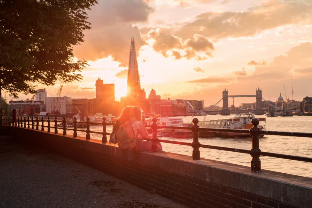 Two women sitting on the river wall over looking the Thames at sunset with the Shard in the background