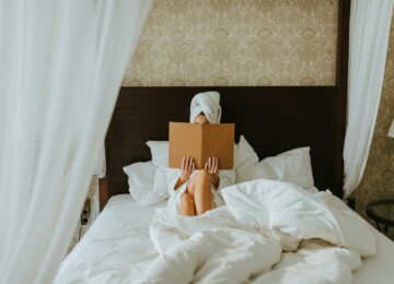 A woman reads while sat in a large hotel bed