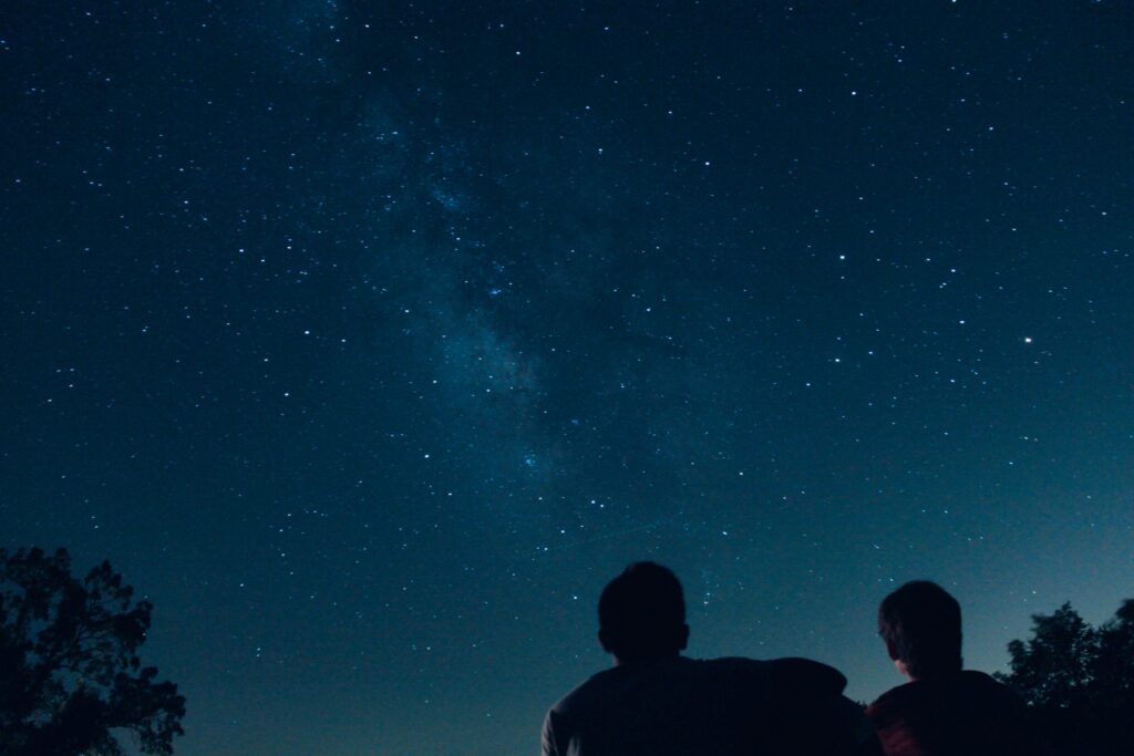 Two silhouettes of people gaze up at the night sky full of stars