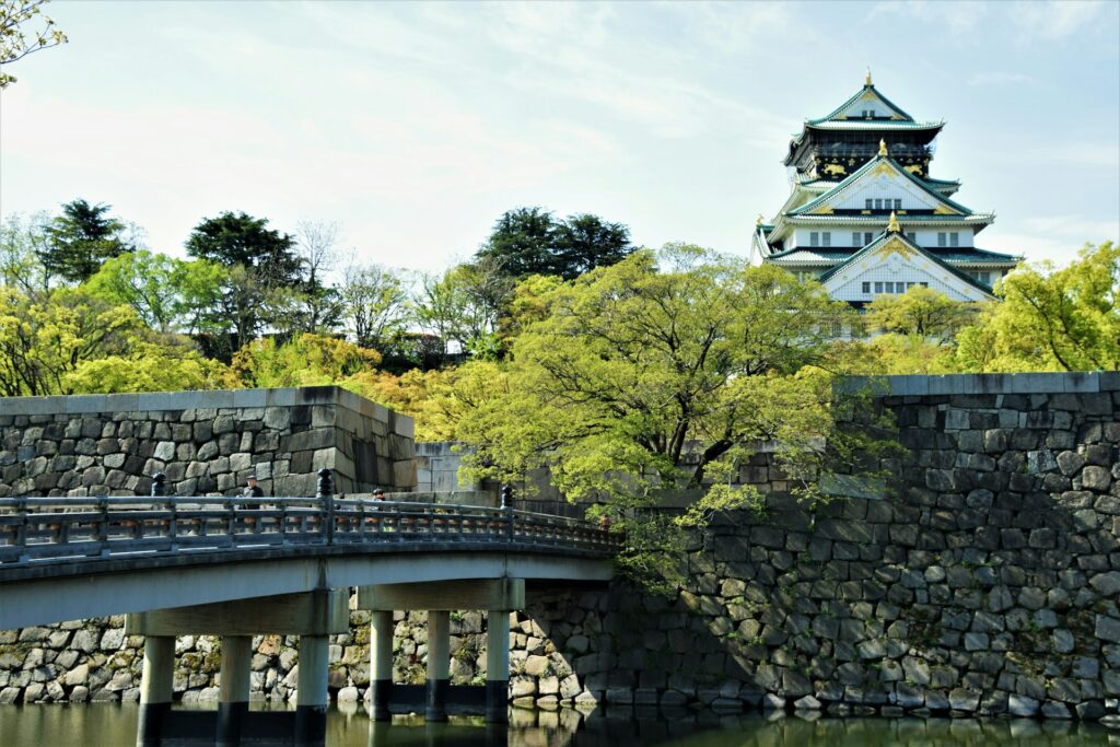 Traditional Japanese temple seen above trees with bridge in the foreground