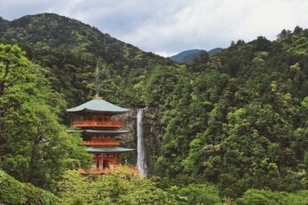 Japanese pagoda surrounded by foliage-covered mountains with a waterfall in the background