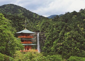 Japanese pagoda surrounded by foliage-covered mountains with a waterfall in the background