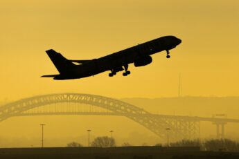 Silhouette of plane taking off with bridge in the background