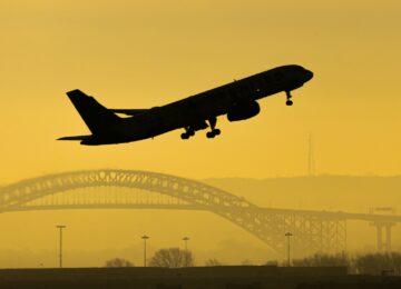 Silhouette of plane taking off with bridge in the background