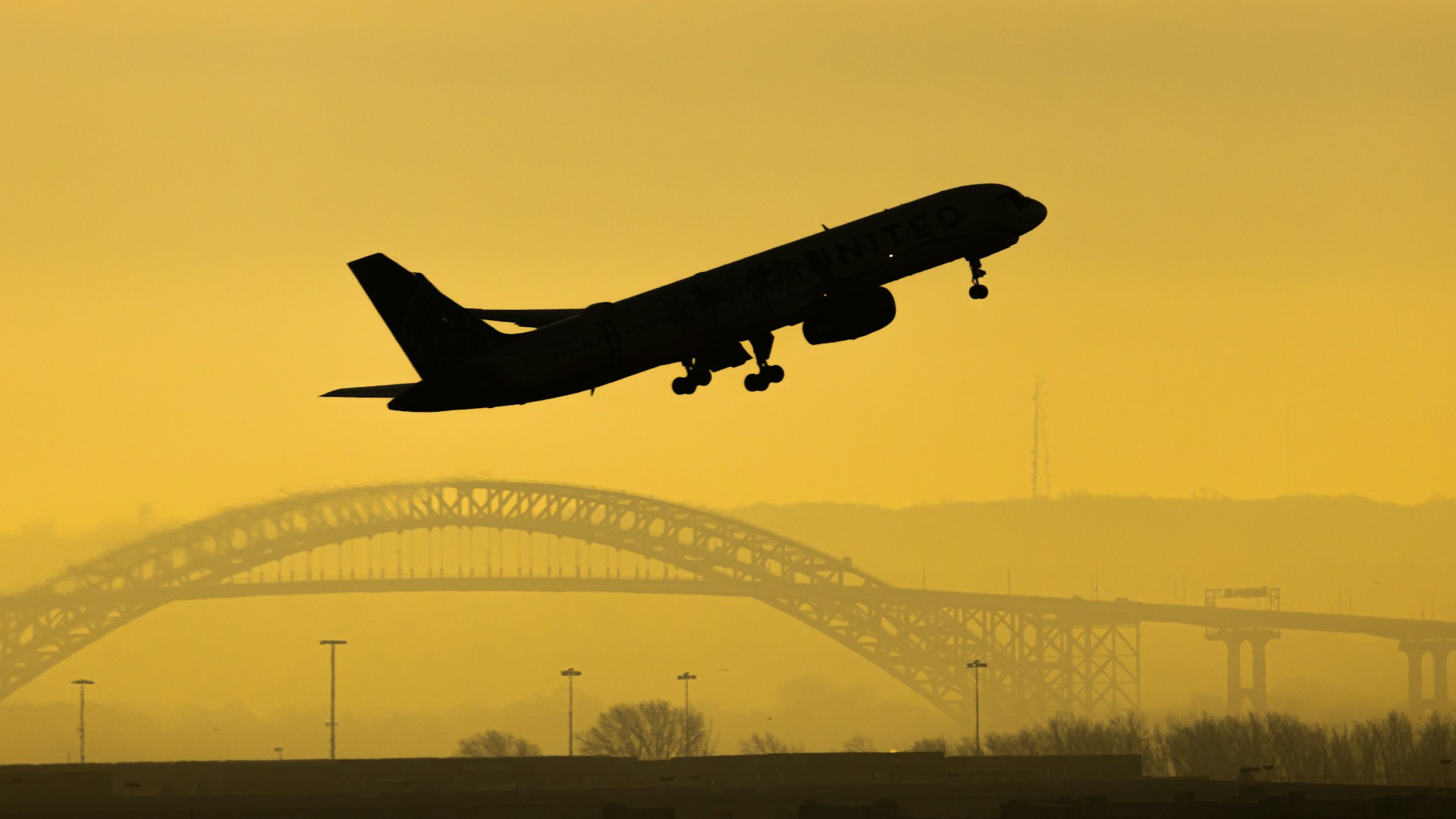 Silhouette of plane taking off with bridge in the background