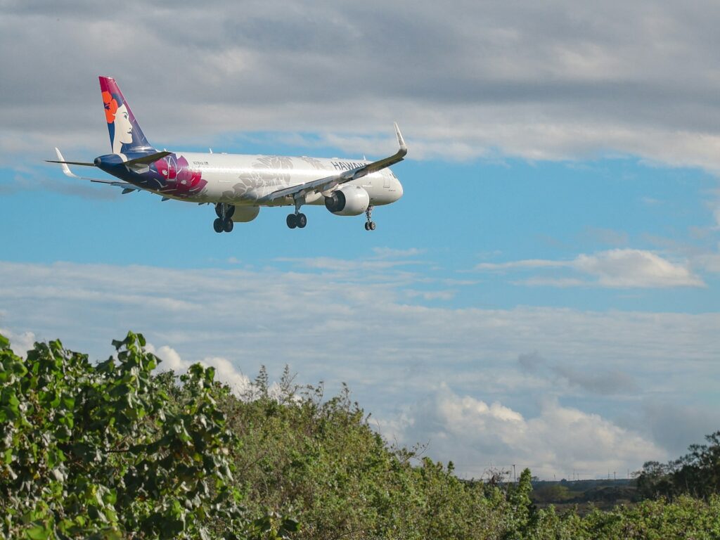 Hawaiian airlines plane landing over green treetops and vegetation