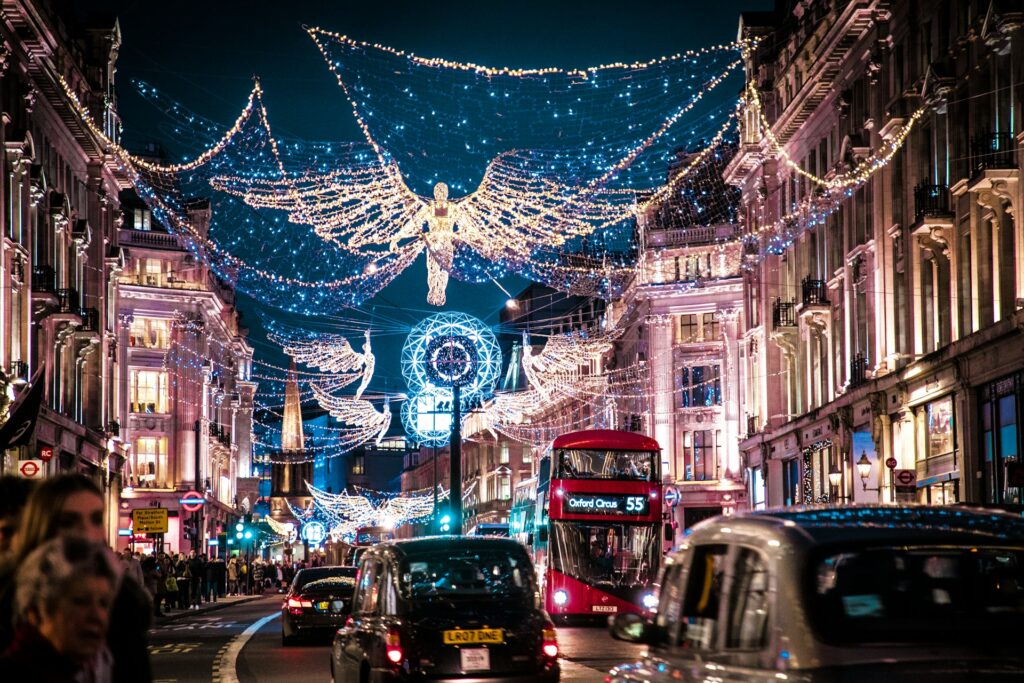 Christmas lights strung above a busy shopping street in London, with double decker bus and black taxi driving beneath