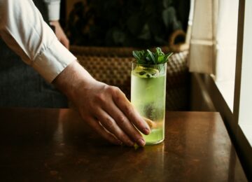 edward-howell-hYcriIw0gHc-unsplash Hand placing green tinted cocktail on a wooden table