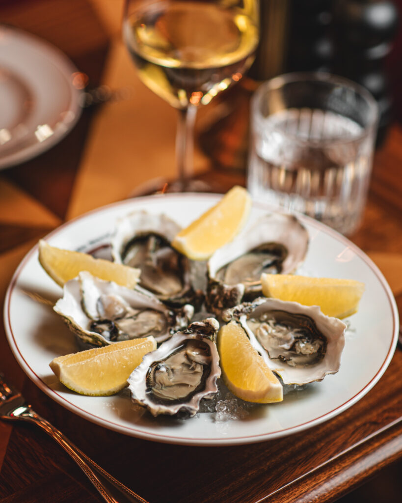 Oysters and lemon slices on a white plate in a restaurant setting