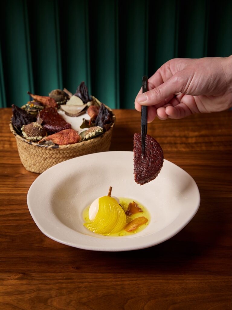 A hand with tweezers placing a chocolate tuille on a dessert