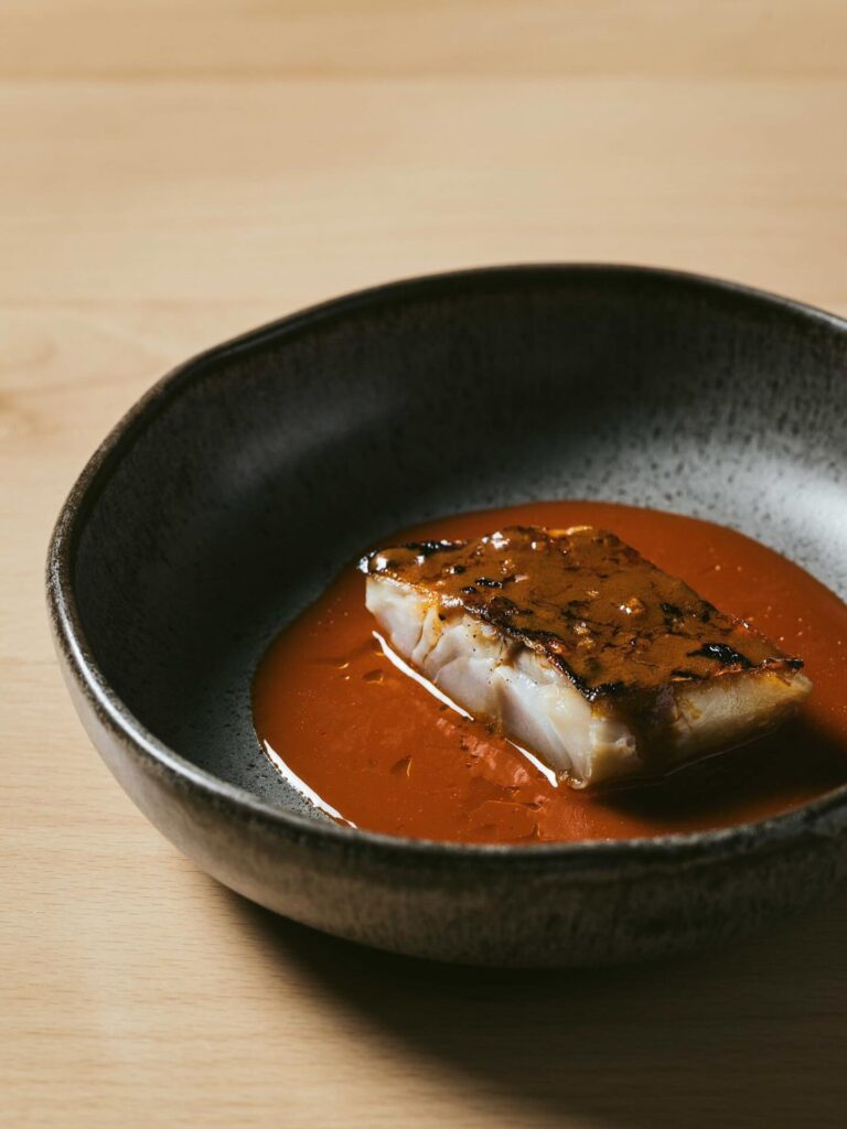 Fish fillet in a dark brown sauce in a black bowl