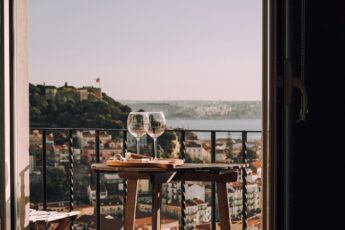 Two wine glasses on a small table on a balcony overlooking Lisbon