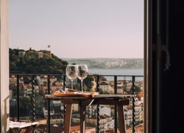 Two wine glasses on a small table on a balcony overlooking Lisbon