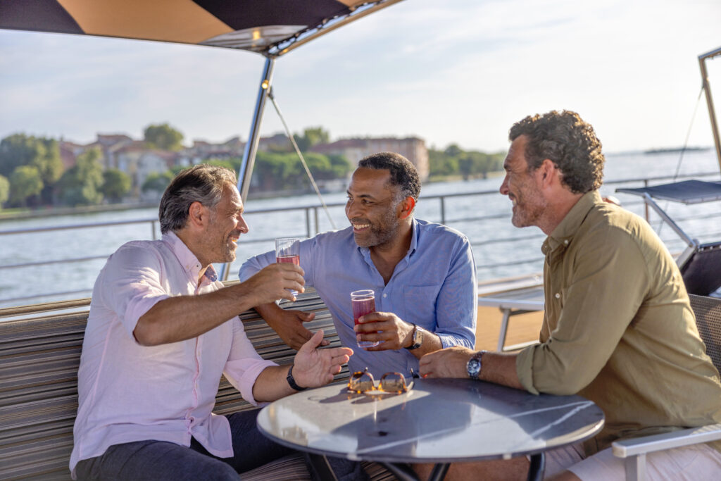 Three men enjoying drinks on the sundeck of the Uniworld ship S.S. La Venezia in the springtime