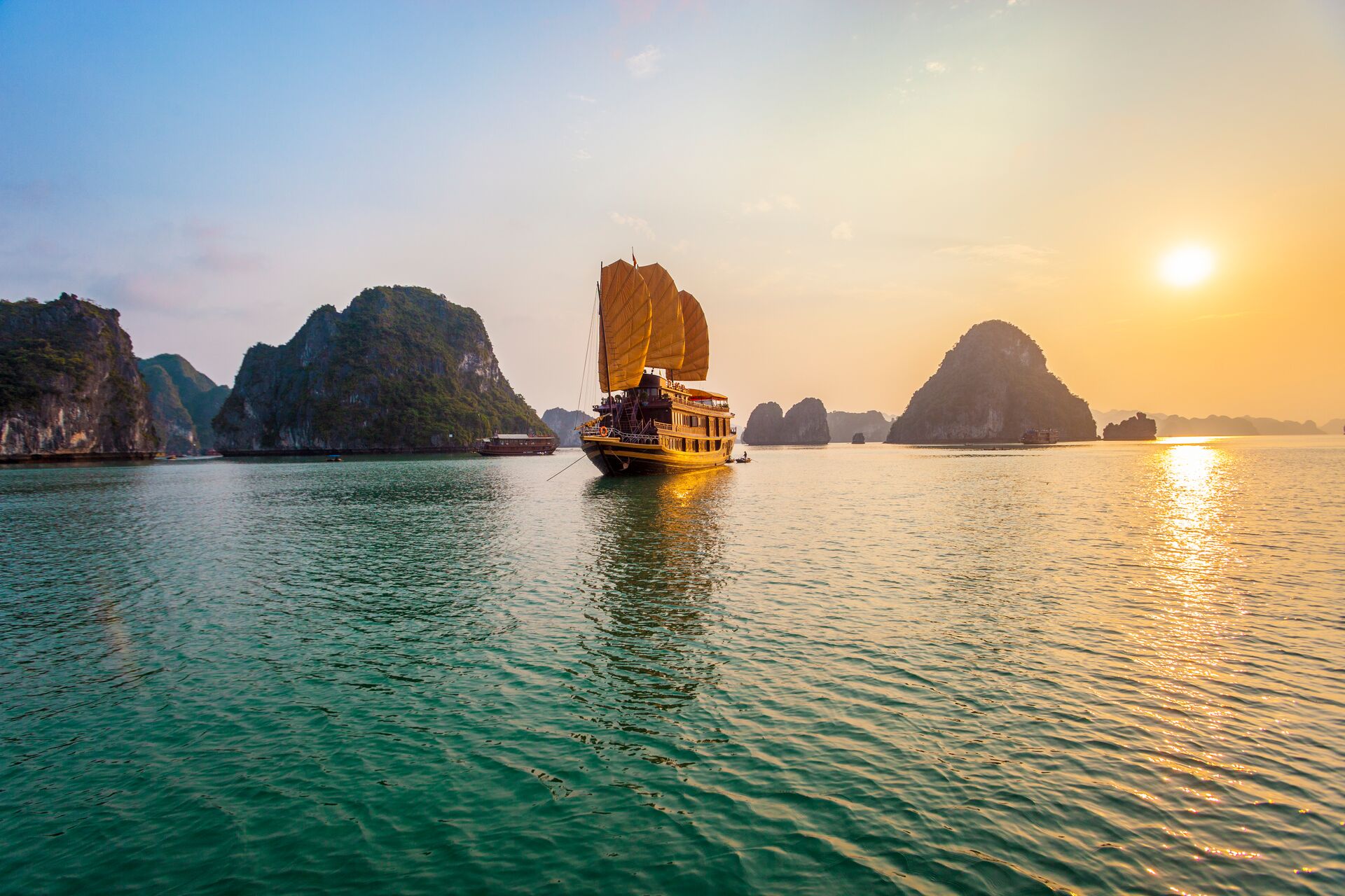 Chinese Junk boat sailing in Halong Bay in Vietnam with the sun setting in the background