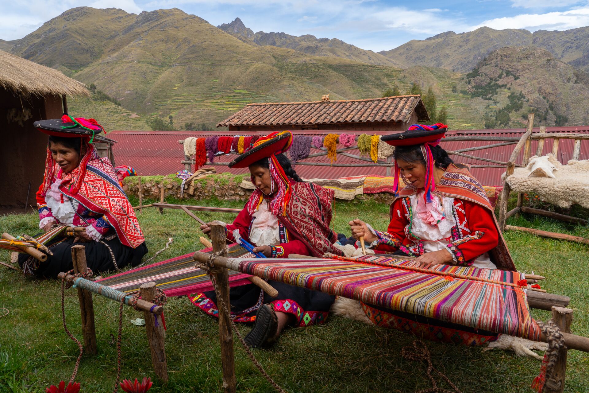 Three local female weavers in colourful traditional local dress including festooned hats, weaving colourful alpaca wool on the ground