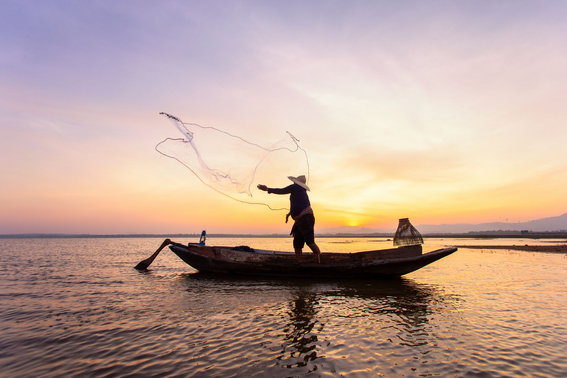 Silhouette of traditional fishermen throwing a net while on a lake at sunrise in Laos