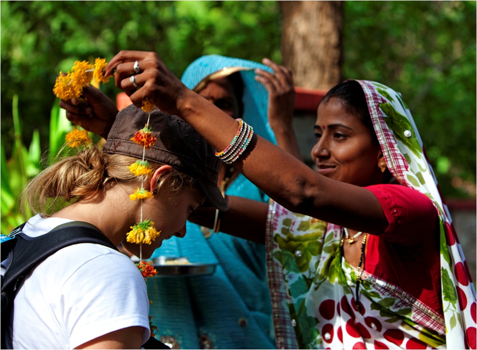 Lady in traditional dress presenting necklace of flowers to tour guest